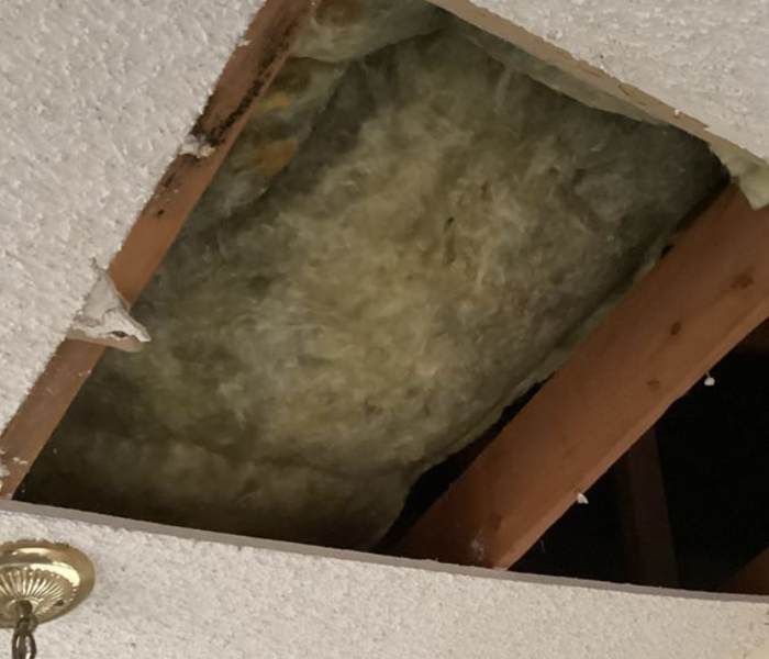 A water-damaged ceiling with a part of it taken out and it has insulation inside